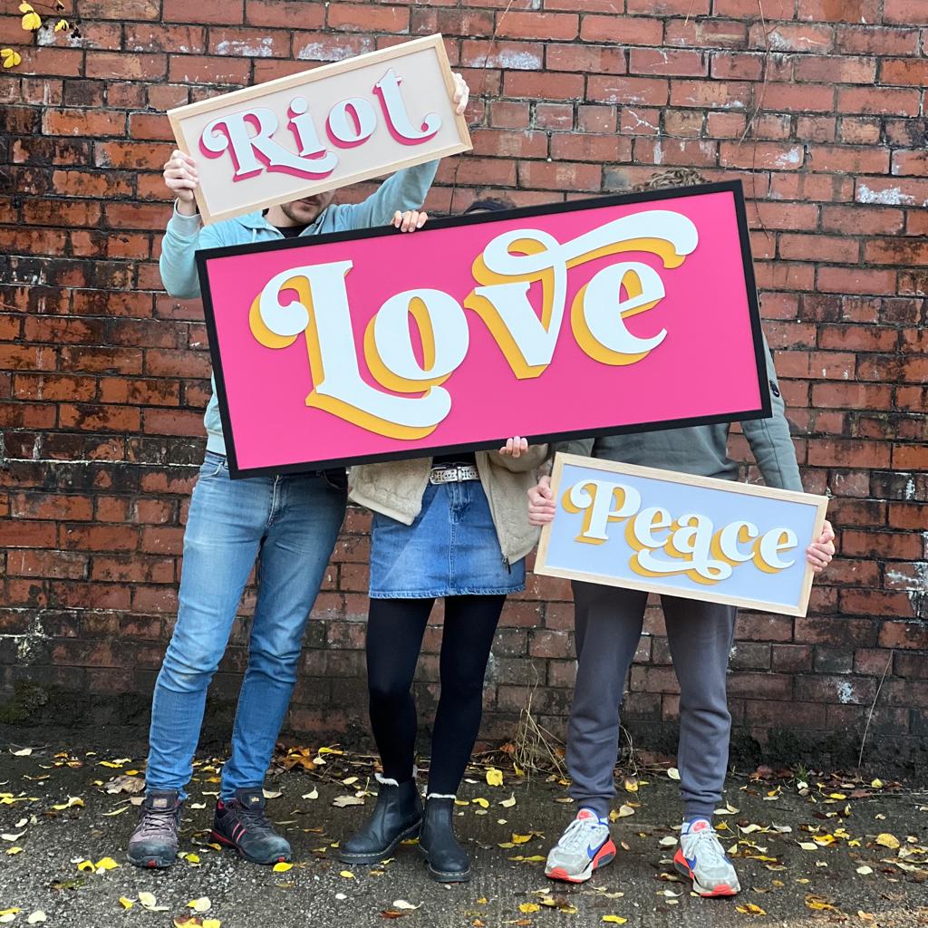 three large wooden signs displaying the words 'Love' 'Riot' and 'Peace' in a vibrant, fancy font