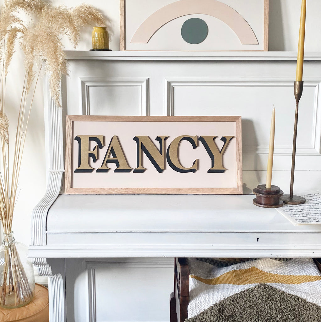 One word painted sign placed upon piano and displaying the word 'Fancy' in gold