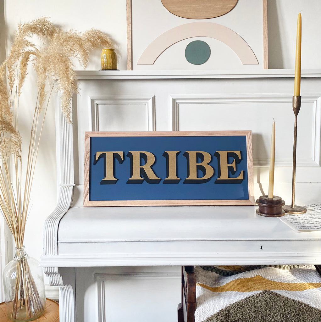 One word painted sign placed upon piano and displaying the word 'Tribe' in gold