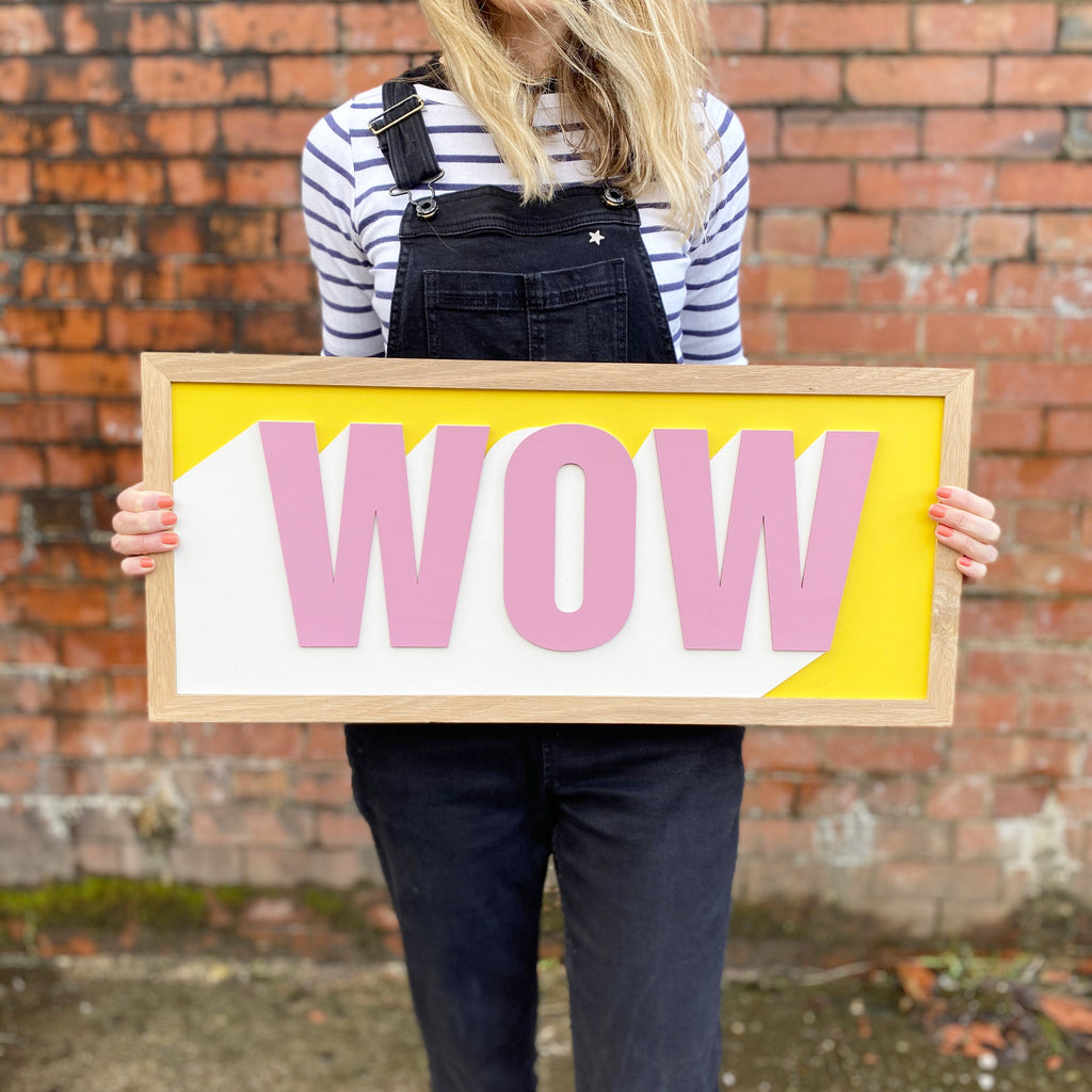Hand painted one word layered sign. the word 'wow' in pink with yellow and white backdrop