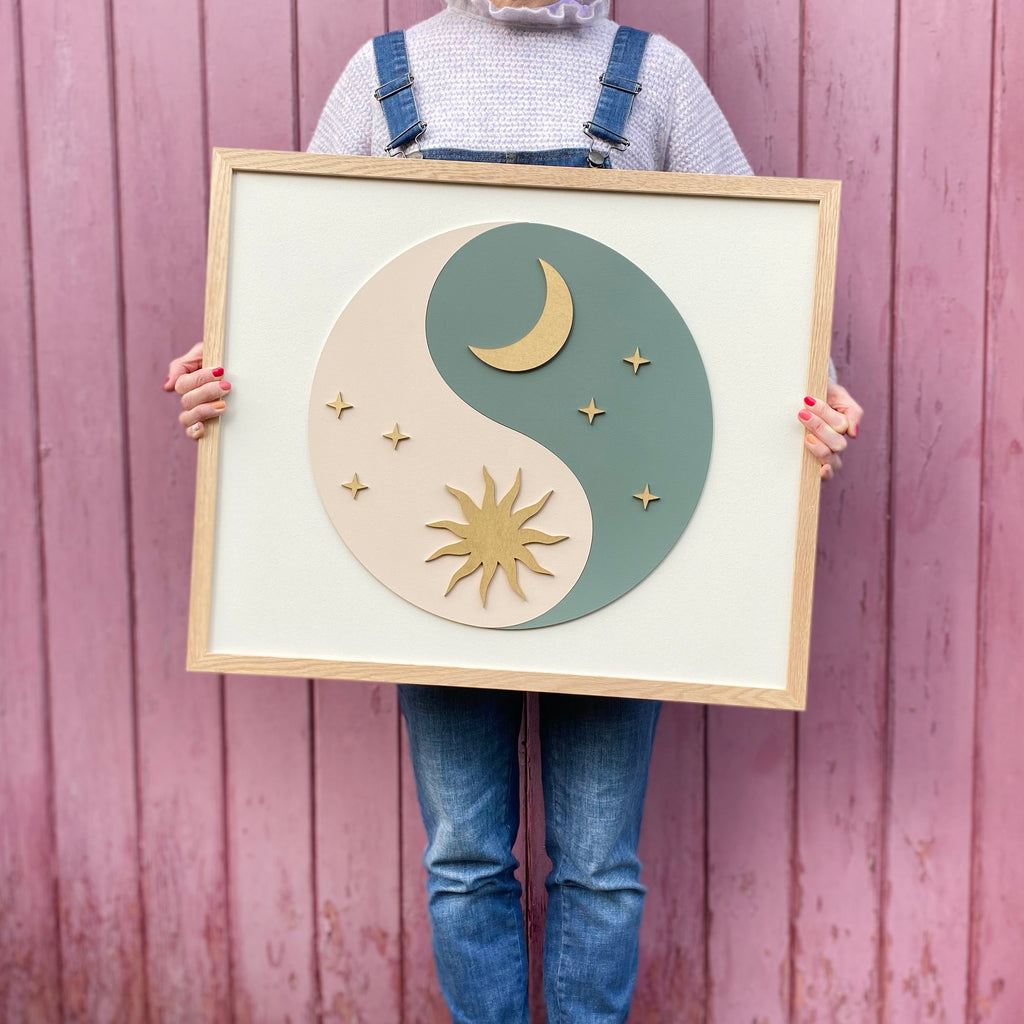 hand painted layered wooden sign with yin yang on painted wood. yin is shown by a pastel green colour with a crescent moon and yang is shown through a cream colour with a sun on top