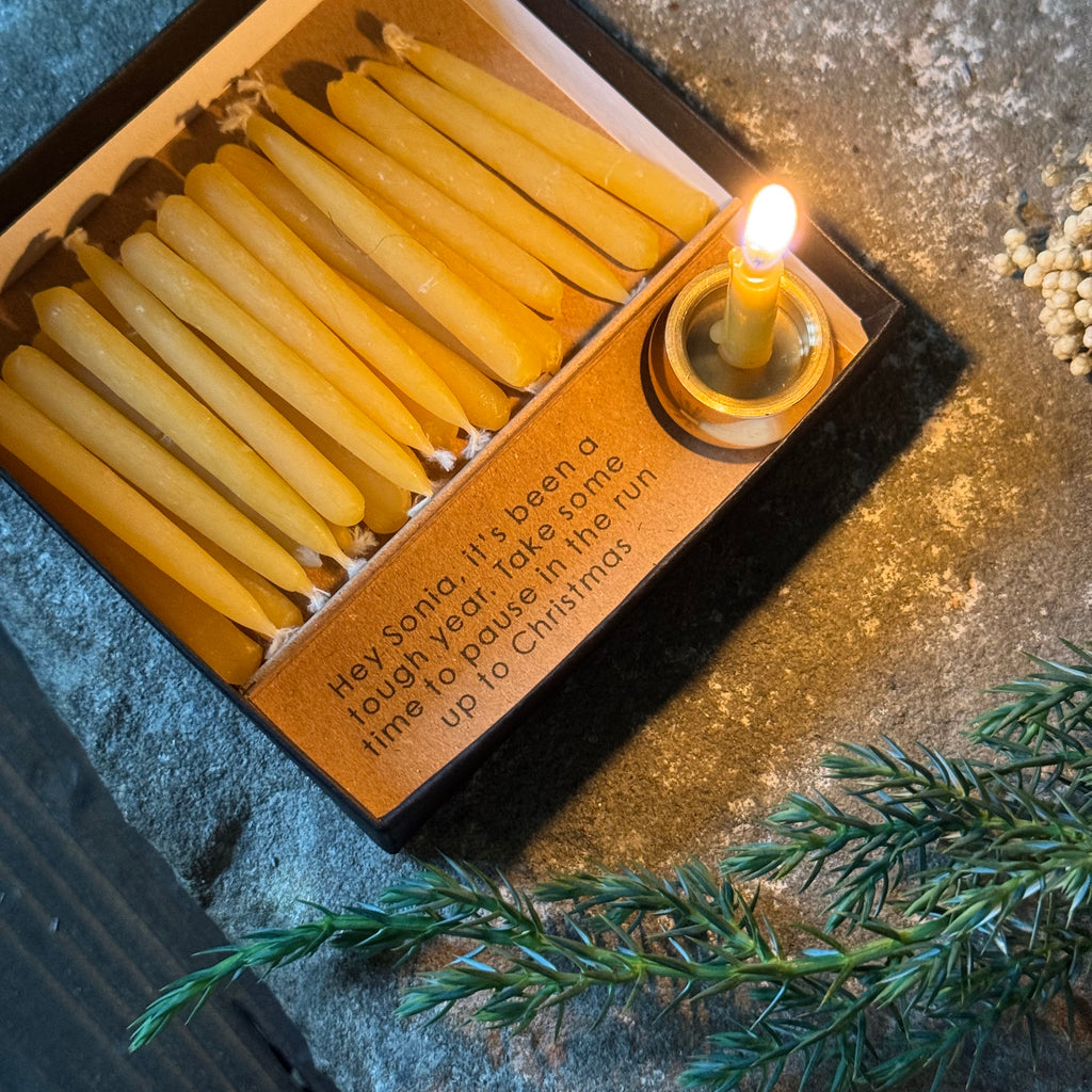 Box of mini mindful® candles with a lit candle next to greenery on a textured surface by modo creative