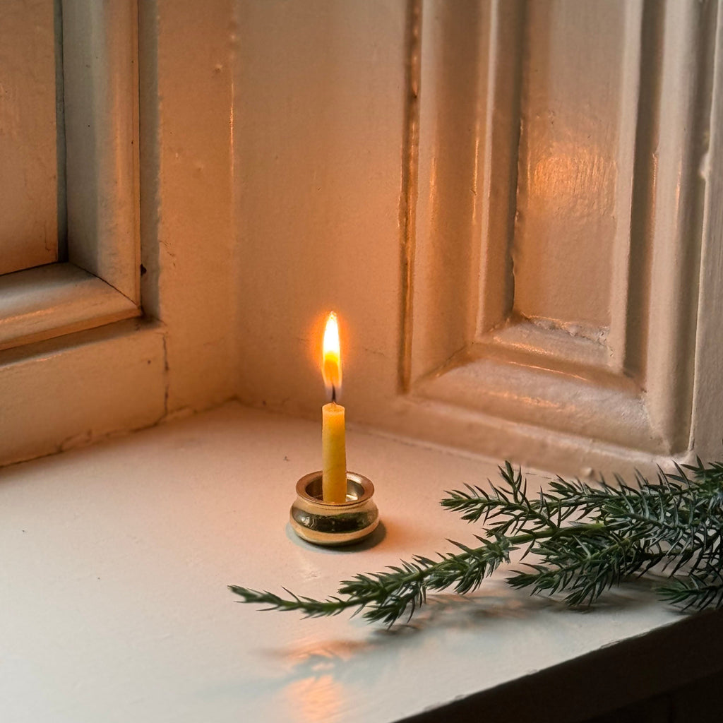 Candle in a holder with a green branch on a windowsill. simple advent beeswax candle