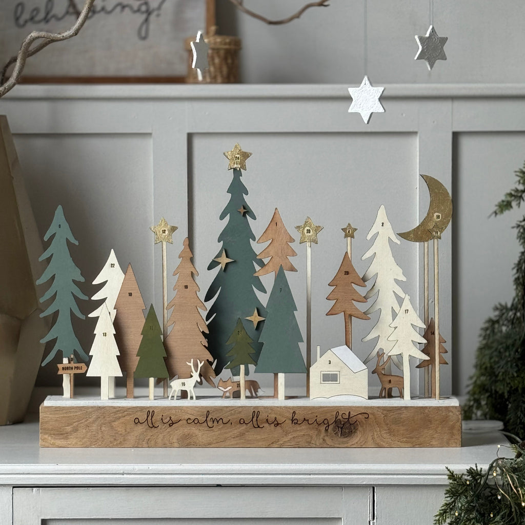 Decorative wooden Christmas trees forest scene and ornaments on a shelf with a neutral festive muted background.