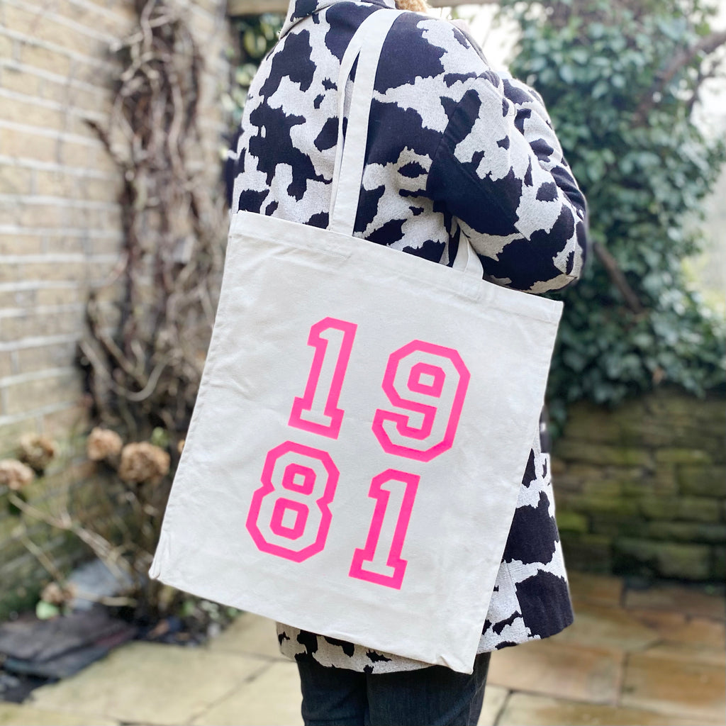 cream over shoulder tote bag with neon pink lettering showing a year. eg 1981