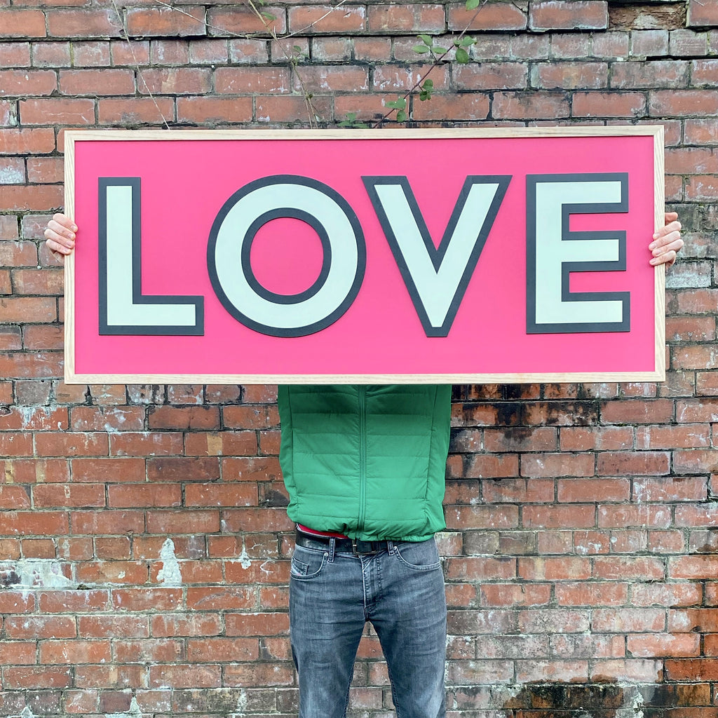 large one word sign with the word love in white lettering. a black outline shadow is around the word along with a vibrant red around the word