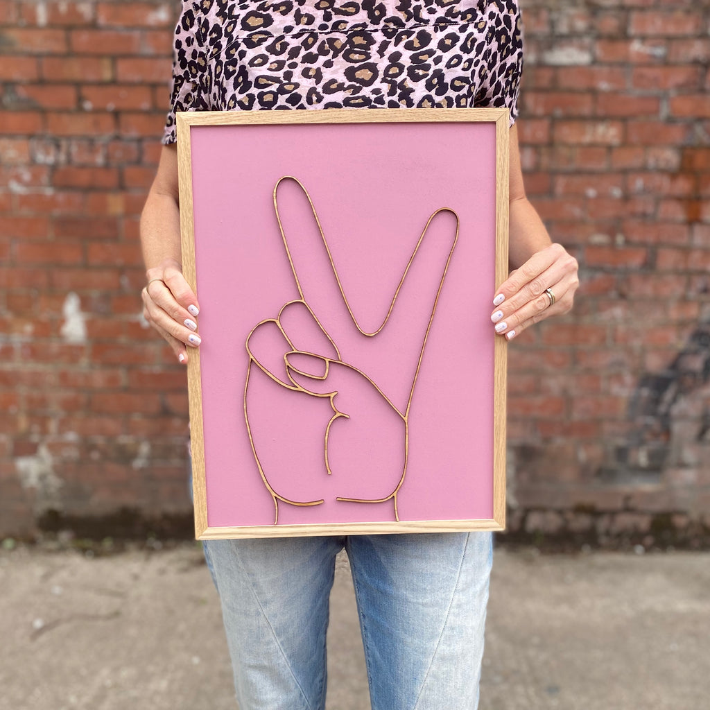 wooden sign hand painted pink with peace gesture over in wood