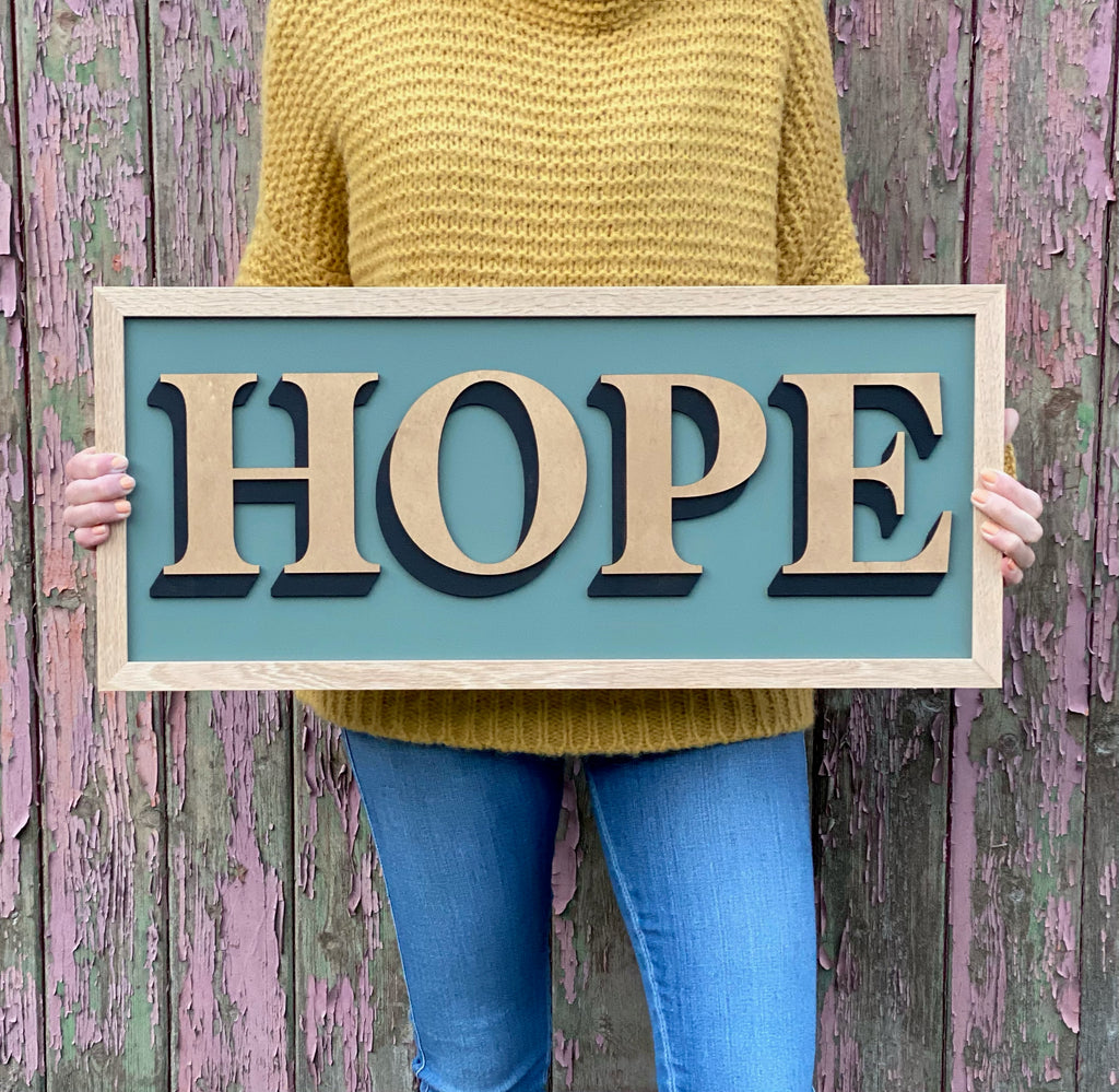 One word Sign displaying the word 'Hope' in gold, being held by a person