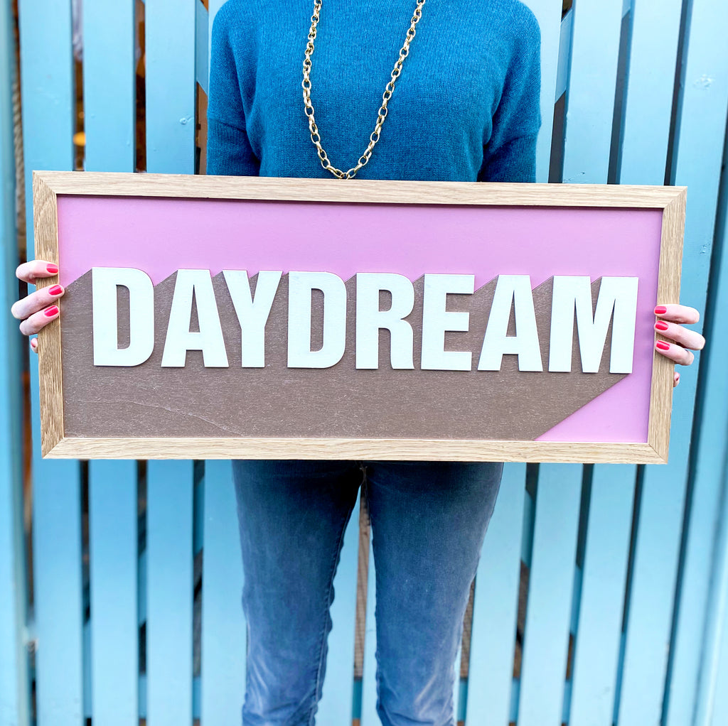 the word 'daydream' on a one word, hand painted layered sign. the colours brown, pink and white used