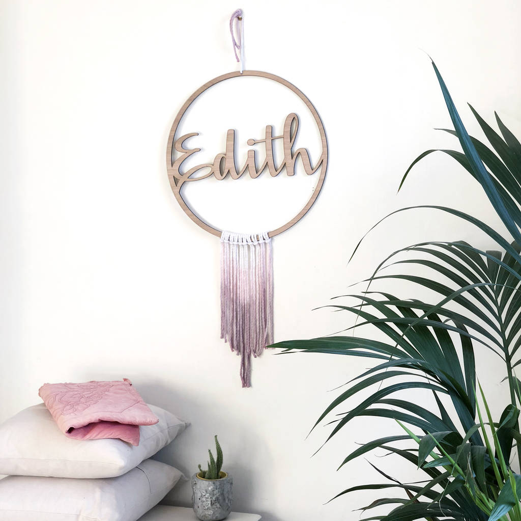wooden circular sign with word in the middle. pink dyed string creating a gradient fade makes the sign resemble a dream catcher.